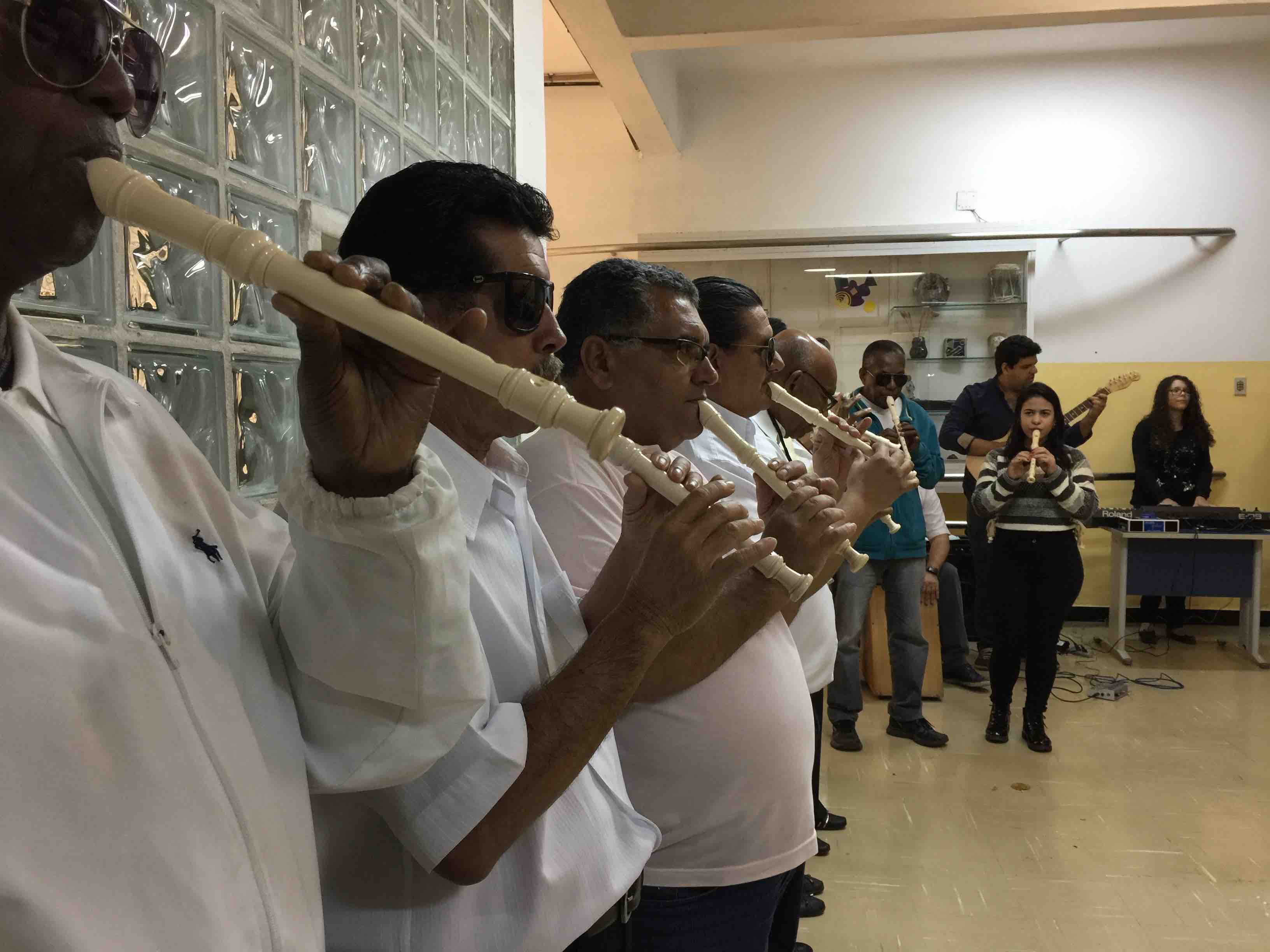 Descrição da imagem: adultos, alunos da Reabilitação do IBC, perfilados, tocando flauta doce em apresentação no saguão de entrada do Instituto.