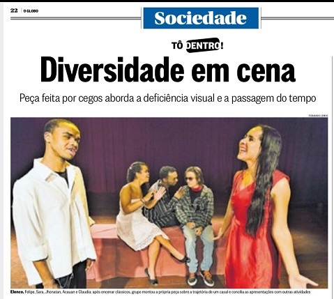 Descrição da foto: imagem de uma foto de jornal com o título "Diversidade em Cena" e subtítulo "Peça feita por cegos aborda a deficiência visual e a passagem do tempo,  Em primeiro plano, vê-se um rapaz e uma moça interagindo; ao fundo, uma moça e dois rapazes também conversam.  A cena se passa num palco.  Abaixo da foto, consta a legenda no qual está escrito: "Elenco: Felipe, Sara, Jhonantan, Acauan e Cláudia: após encenar clássicos, gruppo montou a própria peça sobre a trajetória de um casal e concilia as apresentações com outras atividades". 