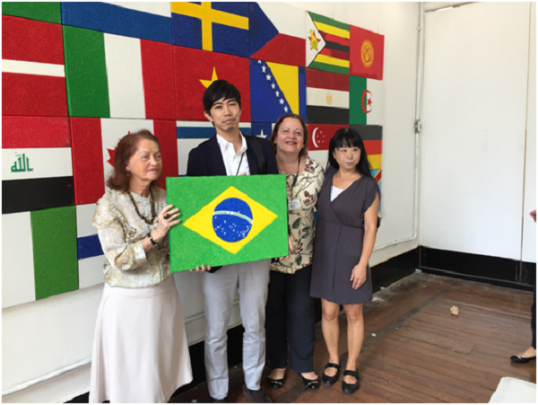 A professora Maria da Glória Almeida e o vice-cônsul do Japão Eiji Takeya posam para a foto segurando a tela com a pintura bandeira do Brasil, ao lado da chefe de gabinete do IBC, Érica Deslandes, e da artista plástica Liku Takahashi.