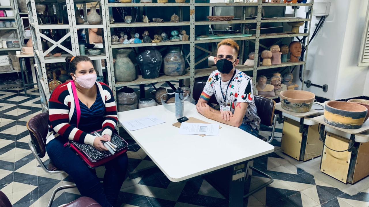Foto na sala de cerâmica com a aluna Iris Bitarães sentada ao lado do professor Rodrigo Agrellos Costa